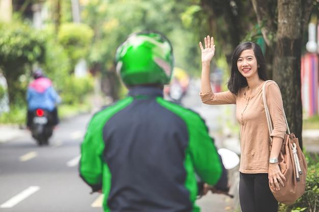 Woman standing on sidewalk ordering motorcycle taxi